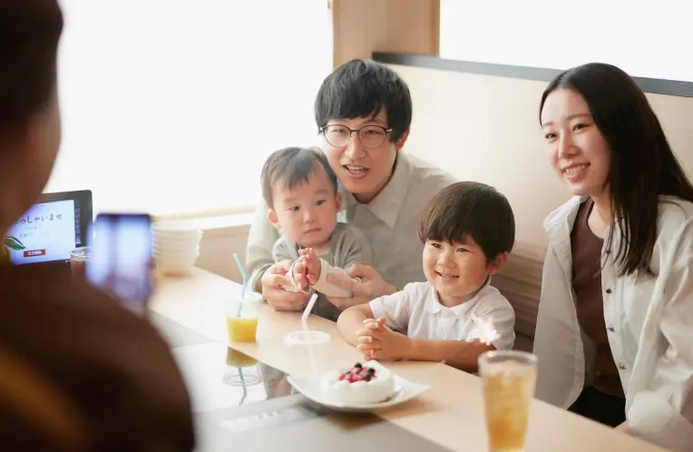 家族が誕生日ケーキを囲み、スマートフォンで記念撮影をしている